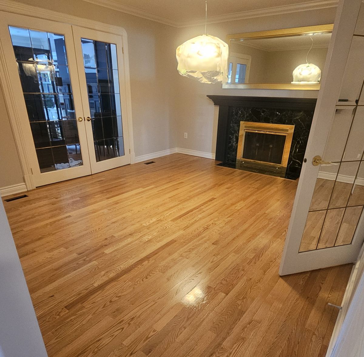 Freshly refinished oak strip flooring in an empty Ottawa living room with a fireplace and French doors
