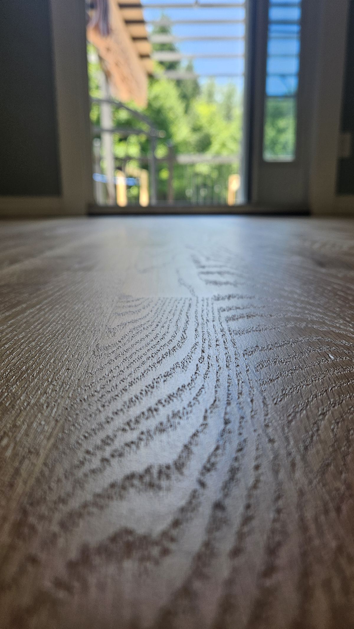 Close-up of a freshly sanded oak floor, the open grain running away toward a sunlit doorway